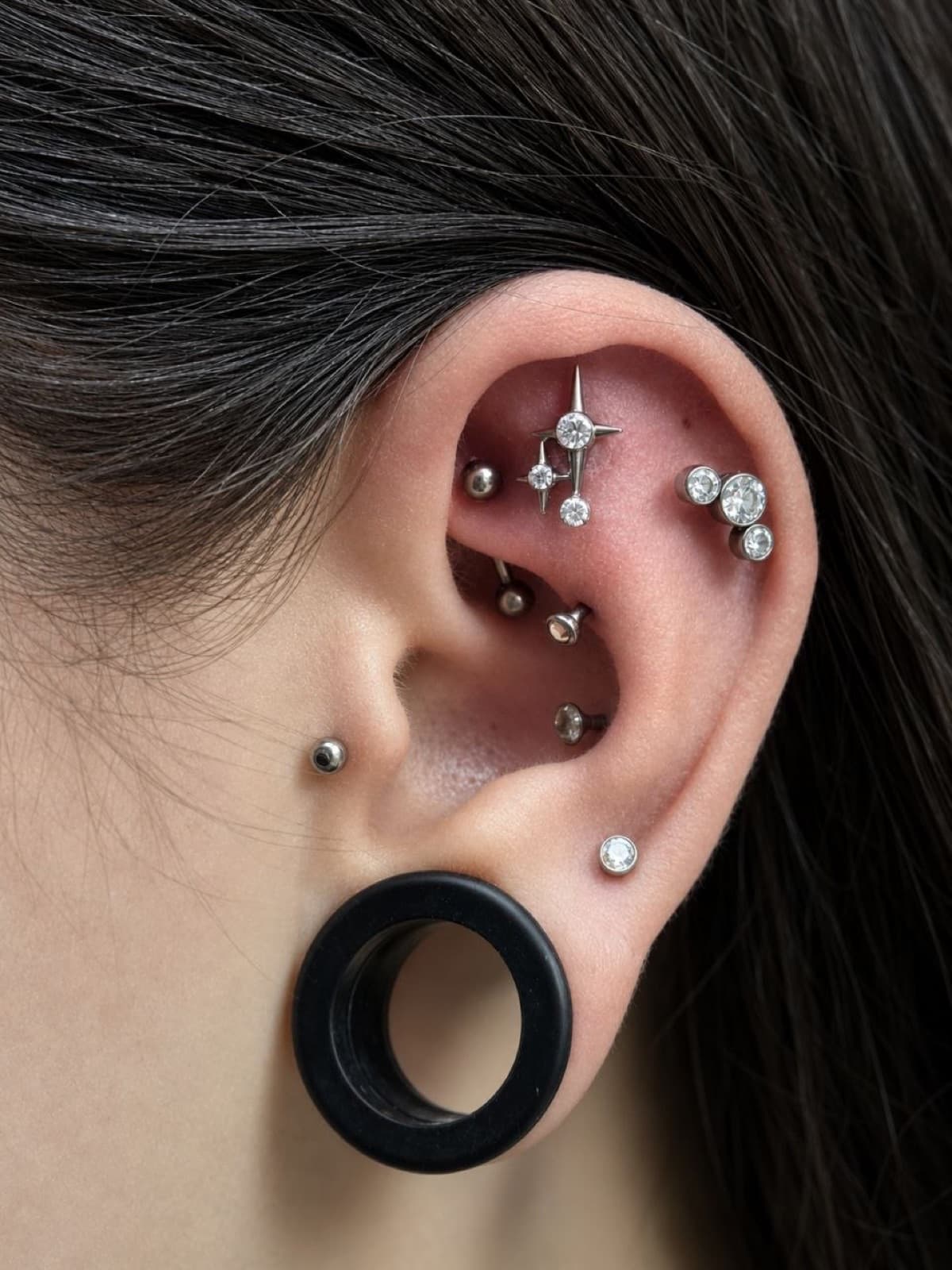 Helix and tragus ear piercings with a starburst charm, ball stud, and black plug